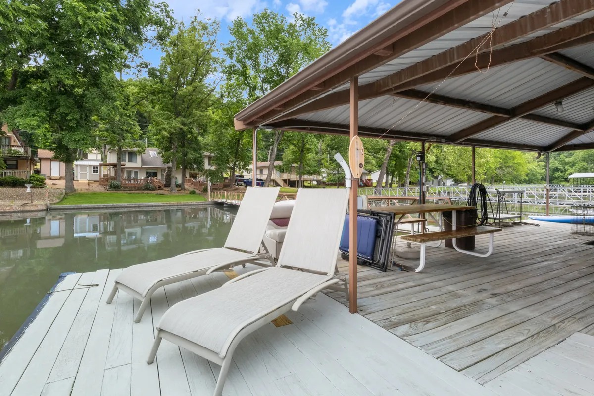 This exterior image features lounge chairs positioned on a dock extending over the water, surrounded by lush trees. The tranquil lake setting invites relaxation, with the dock serving as a focal point for sunbathing, fishing, and easy lake access. The scene suggests peaceful mornings or afternoons spent by the water, with the possibility of launching kayaks or paddleboards nearby.