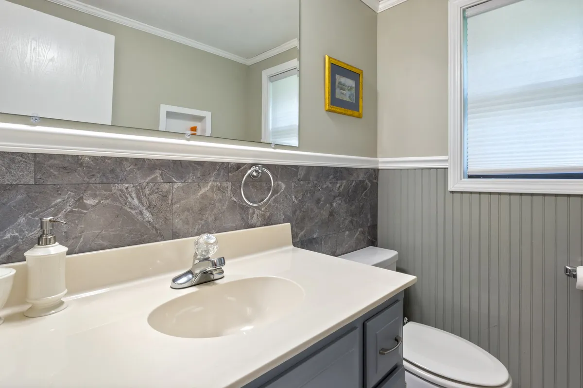 A stylish powder room featuring a vanity sink, mirror, and framed artwork set against soothing gray wall tile. The space feels fresh and calming, ideal for quick touch-ups or moments of privacy.