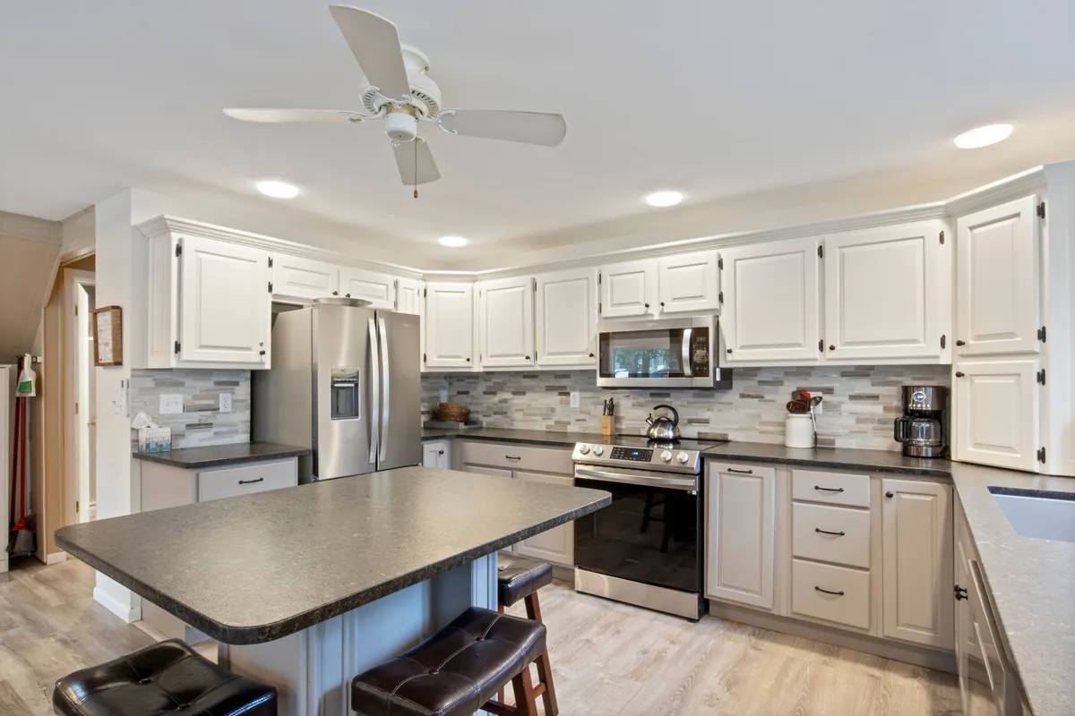 This interior image centers on a bright, well-appointed kitchen featuring a spacious kitchen island, modern stainless steel appliances, and ample cabinetry. The layout suggests plenty of counter space—ideal for meal prep or gathering with family while cooking.