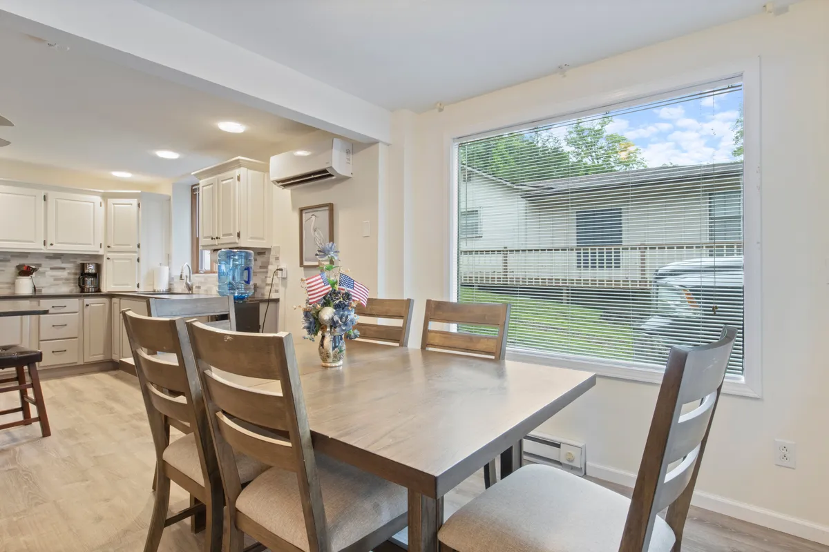 A warm dining area features a wooden table set near a window, with the kitchen cabinetry in the background. The setup is ideal for gatherings, encouraging conversation and connection over meals, with natural light enhancing the cozy ambiance.