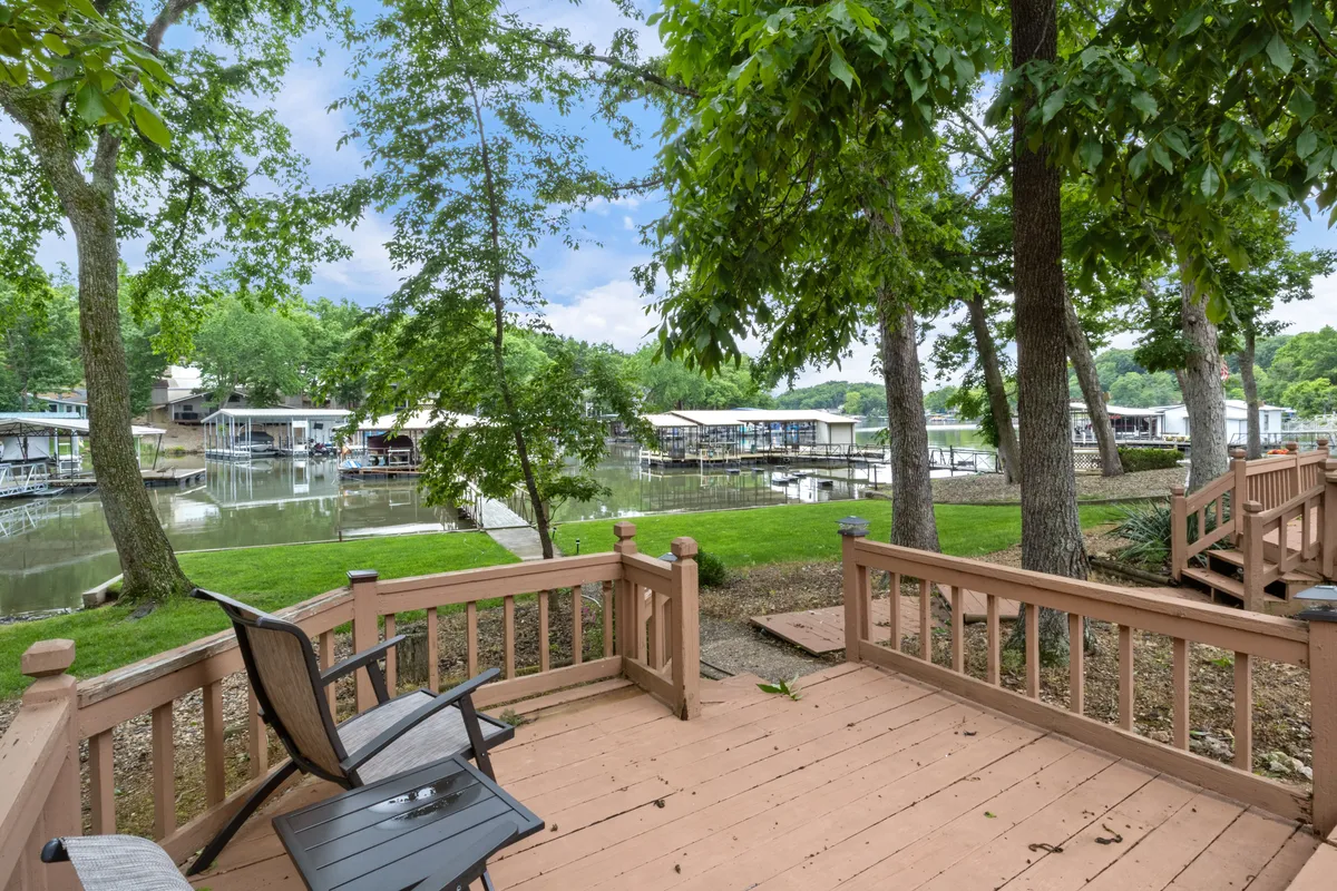 A wide deck overlooks the serene lake, with views of nearby boathouses and surrounded by trees. The space is perfect for morning coffee, relaxing after lake adventures, or simply enjoying the scenic sunset with friends.
