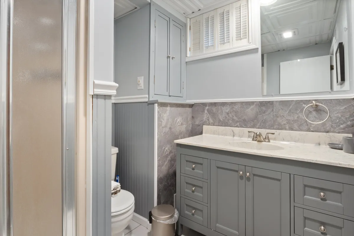 A well-appointed full bathroom with a marble-topped vanity, mirror, glass-enclosed shower, toilet, and ample storage. The calm decor and clean lines create an inviting space for self-care and refreshment.