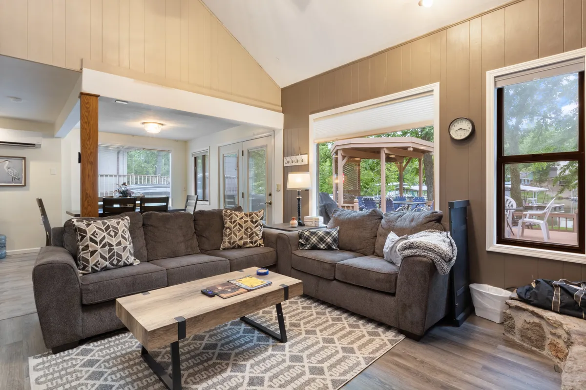 A cozy living area with a plush sofa adorned with decorative pillows, a coffee table at the center, and expansive windows providing breathtaking views of the lake. The space is ideal for relaxing, enjoying coffee, reading, or sharing stories with loved ones while basking in the scenic backdrop.